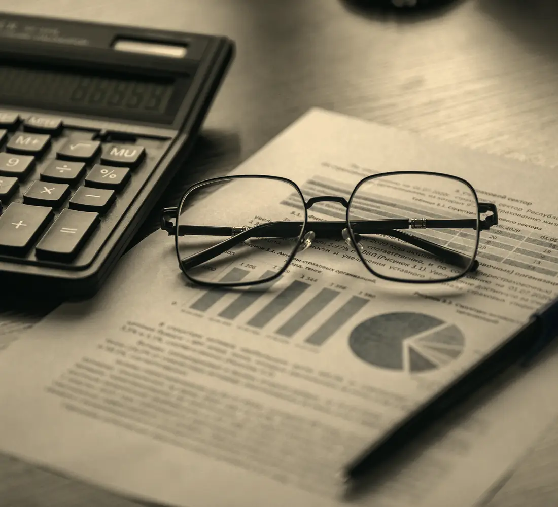 Documento financeiro com gráficos, calculadora e óculos sobre a mesa